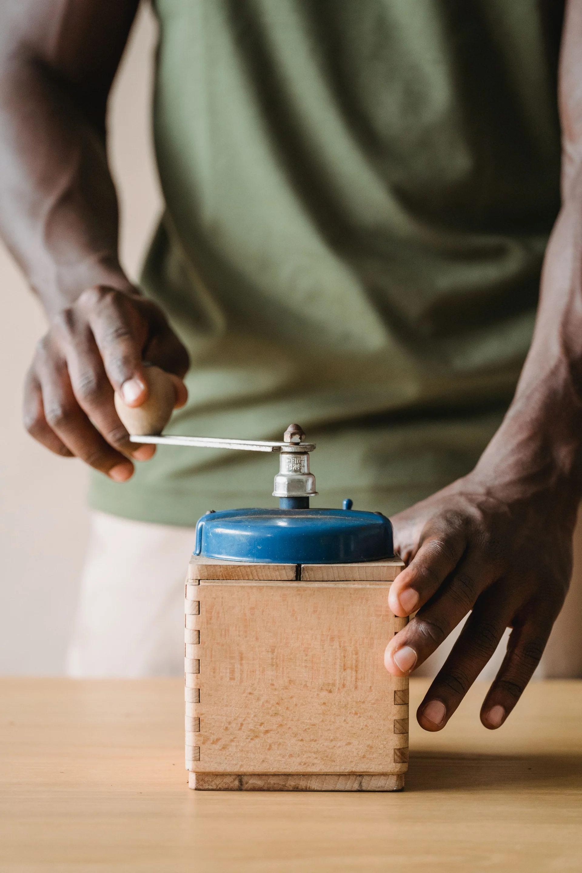 Hands turning a wooden hand-crank coffee grinder.
