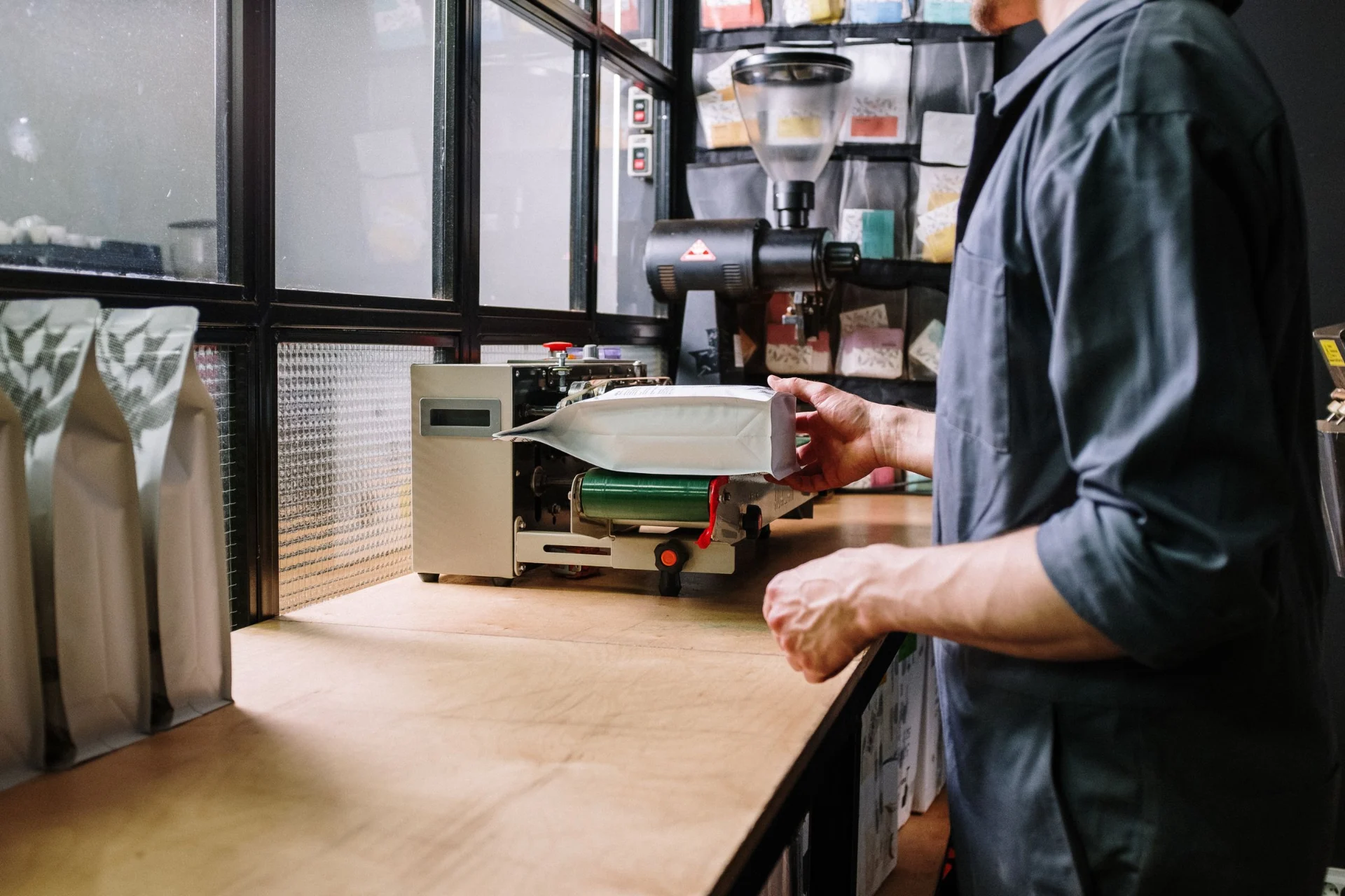 Man in a dark shirt standing at a counter with a machine for filling coffee bags.