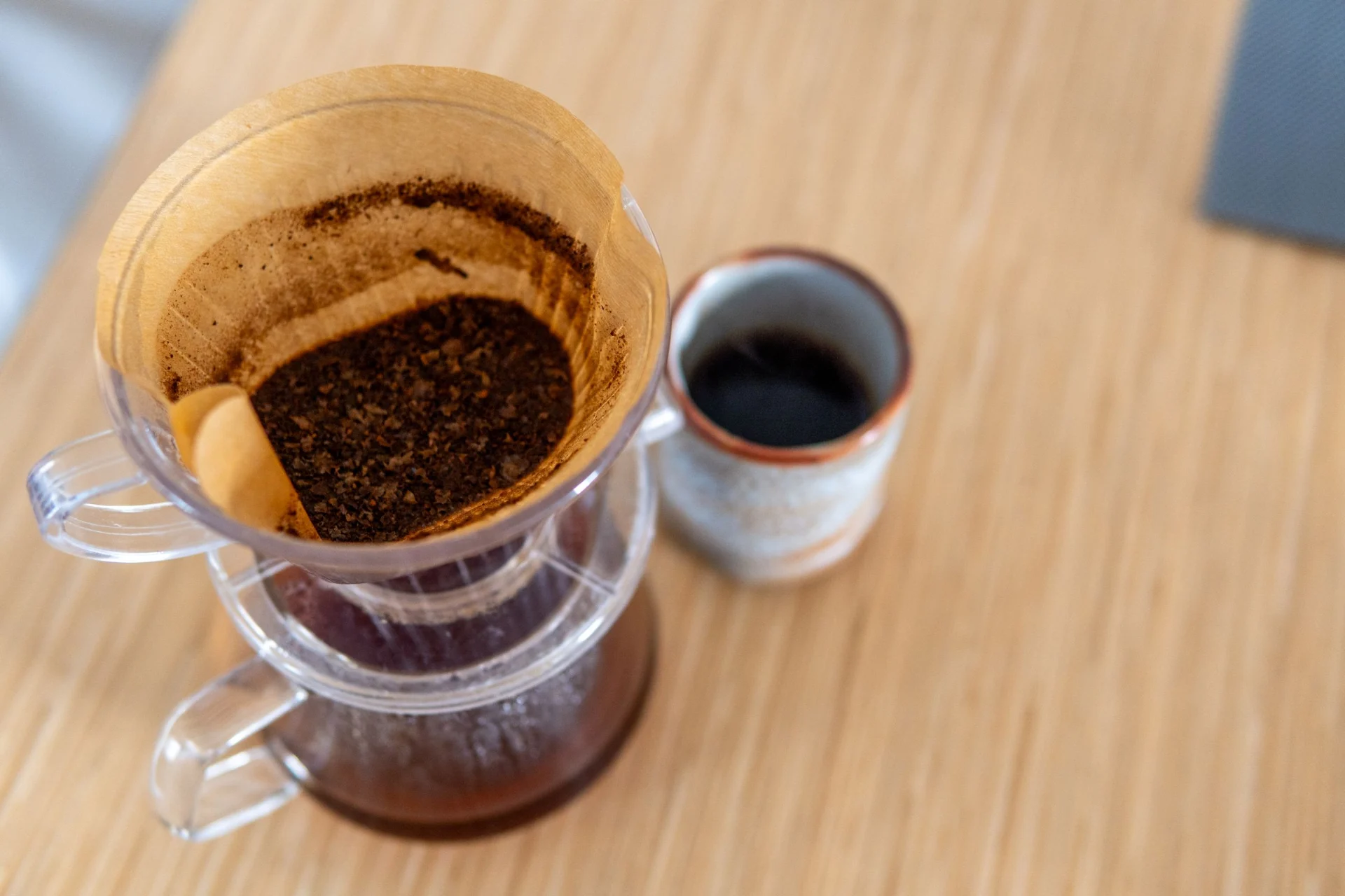A pour-over coffee maker with coffee grounds and a cup of brewed coffee on a wooden table.