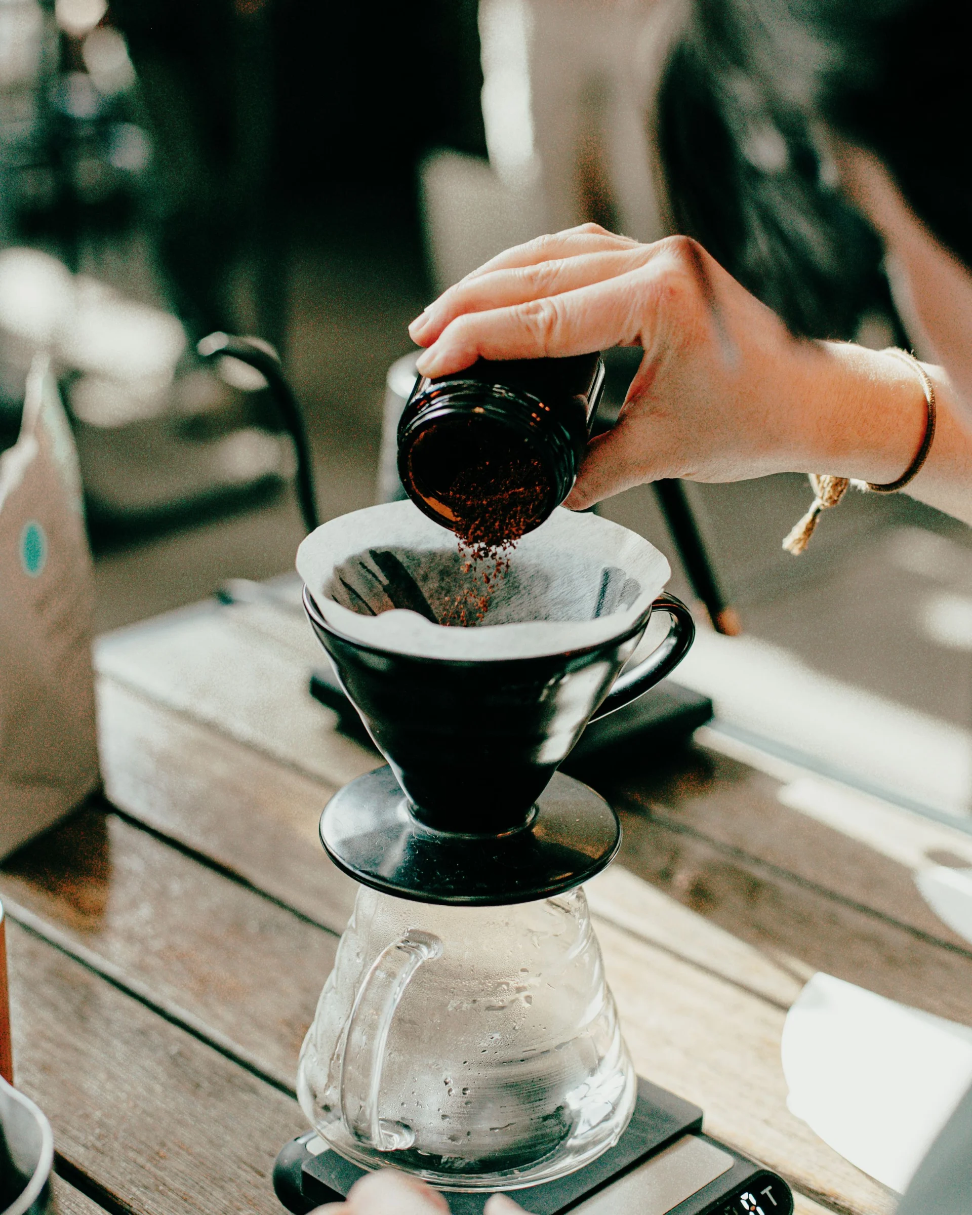 A person pouring coffee grounds into a pour-over coffee maker on a wooden table.