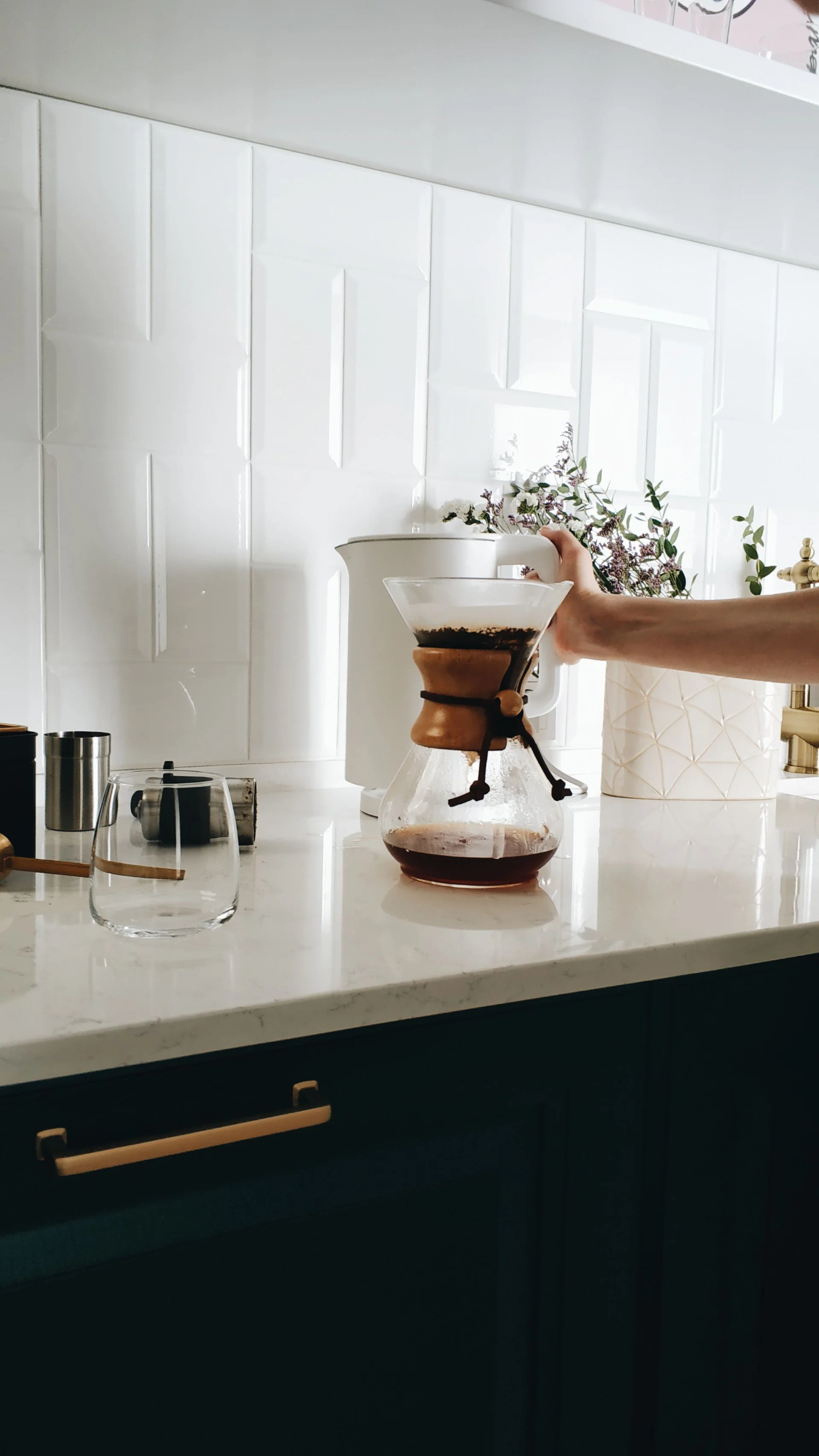 A hand holds a coffee filter over a pour-over coffee maker on a kitchen counter.